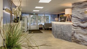 Un espace d’accueil doté d’un comptoir en marbre, d’une grande plante et offrant une vue sur l’extérieur grâce à la porte vitrée.