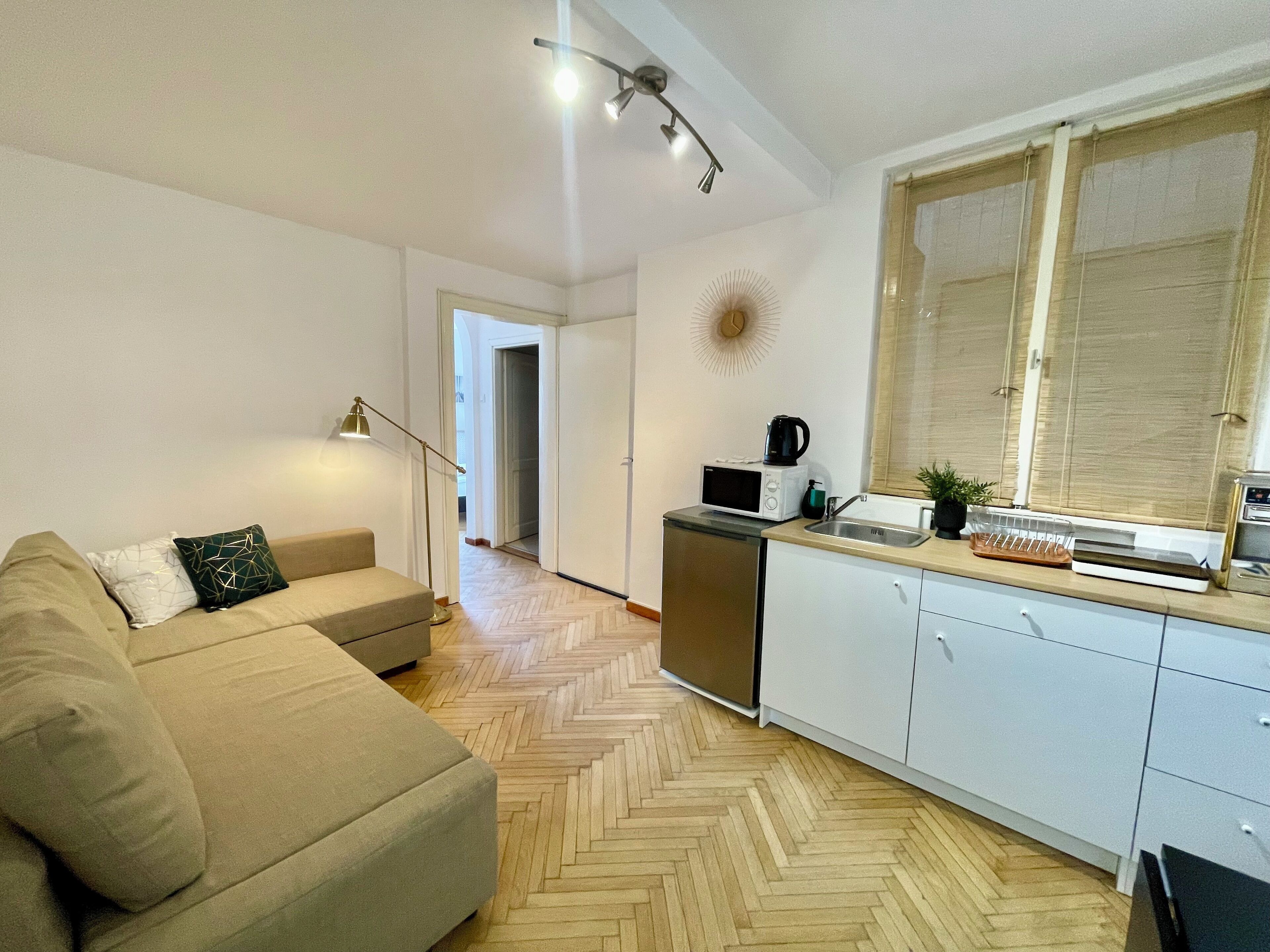 A modern kitchen with a herringbone floor, a microwave, a kettle, and a window with blinds.