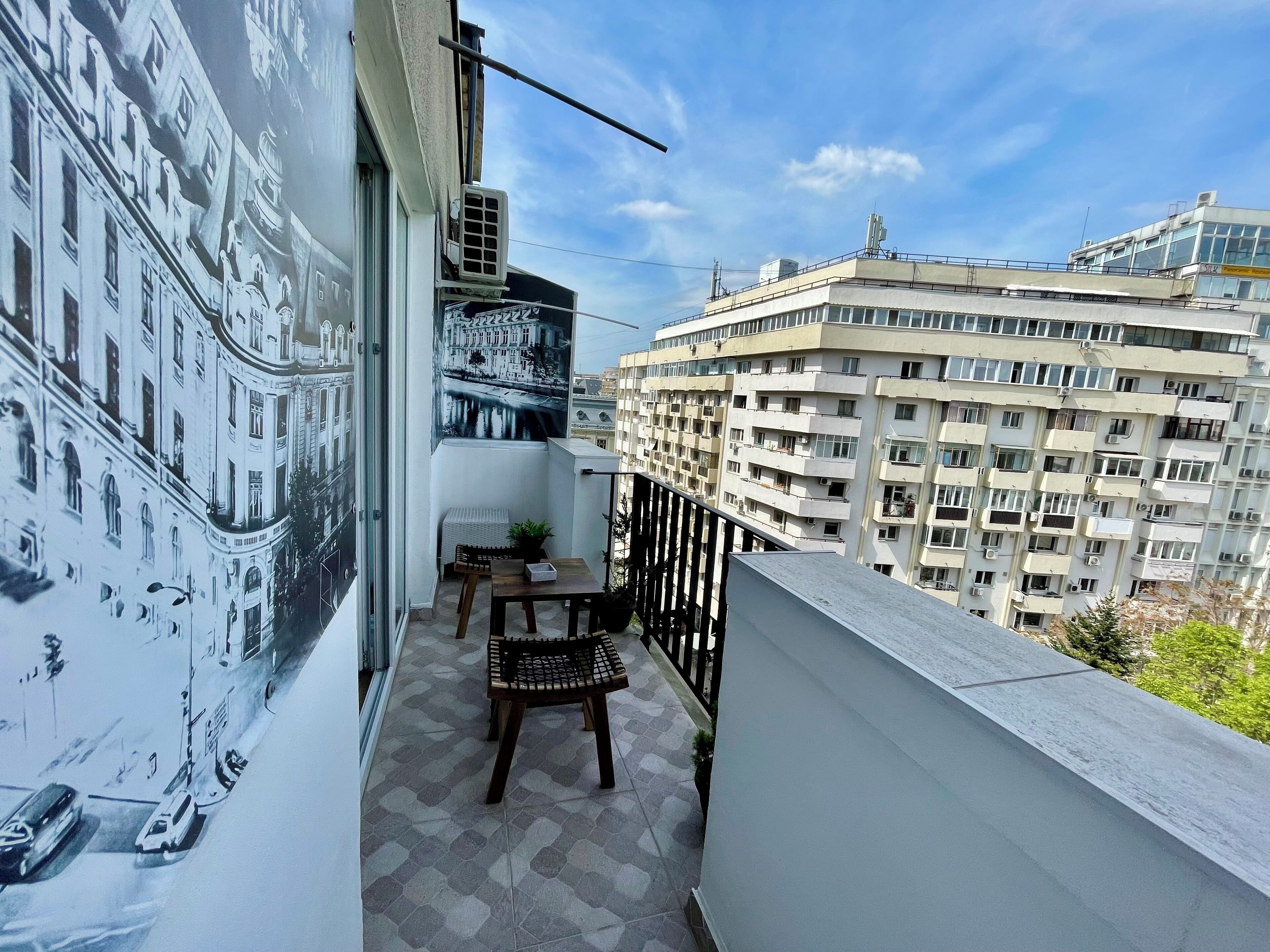 Ein Balkon mit Blick auf eine Stadtansicht, einem Stuhl, einem kleinen Tisch und einer Klimaanlage.