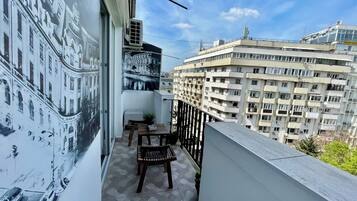 Ein Balkon mit Blick auf eine Stadtansicht, einem Stuhl, einem kleinen Tisch und einer Klimaanlage.
