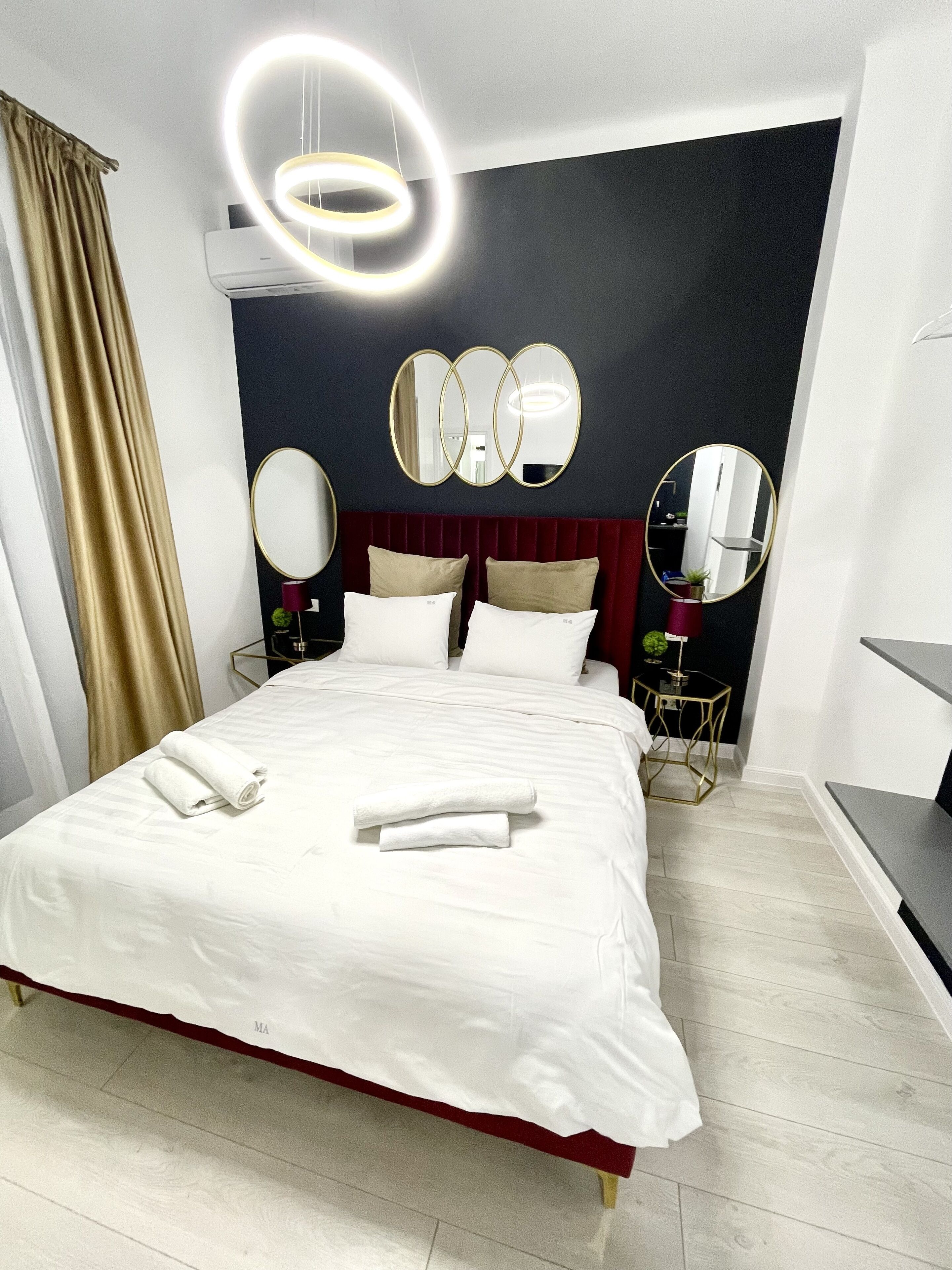 A modern hotel room with a large bed, two bedside tables, a red headboard, and a wall-mounted mirror.