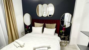 A modern hotel room with a large bed, two bedside tables, a red headboard, and a wall-mounted mirror.
