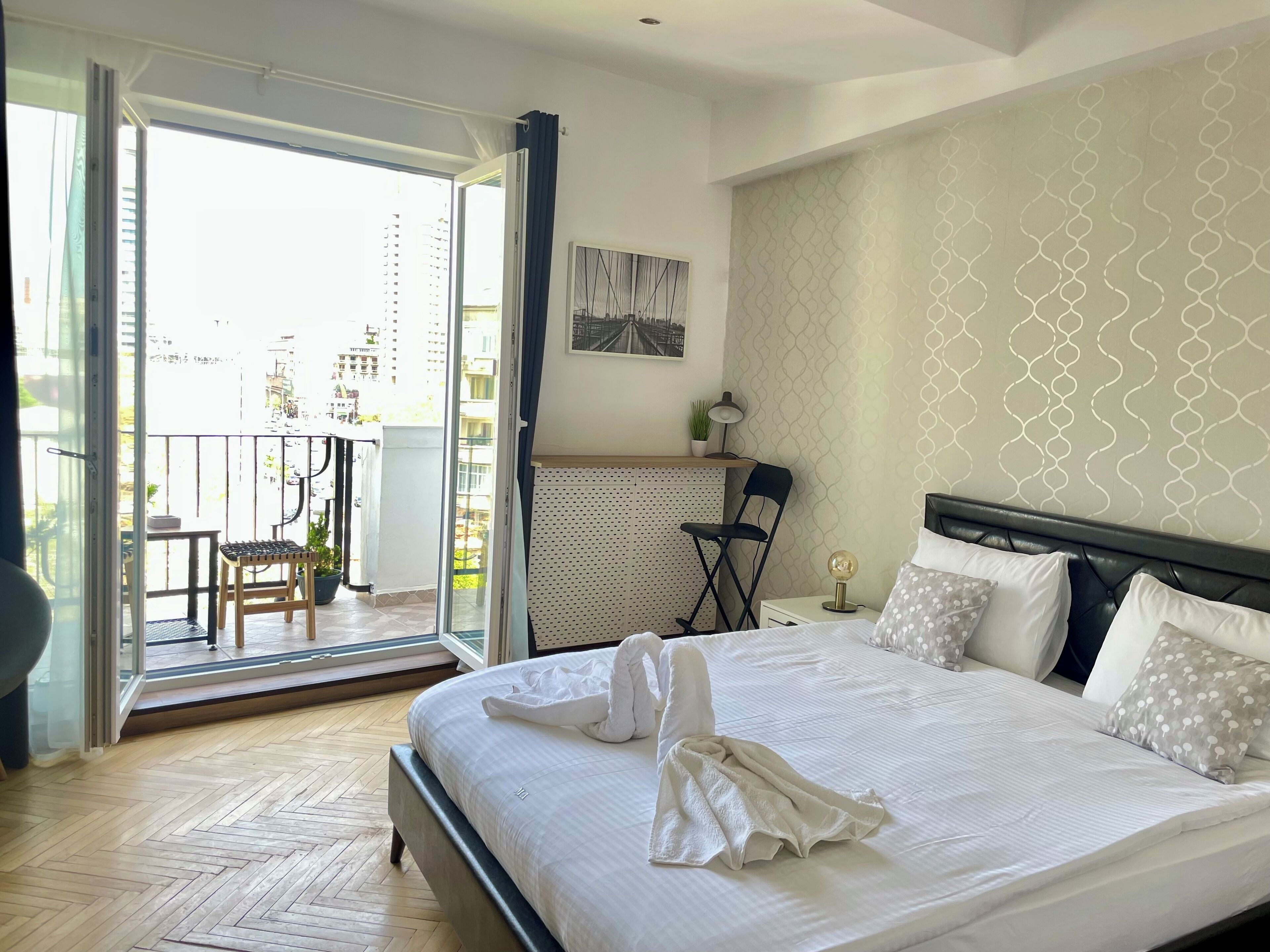 Habitación de hotel con cama, escritorio, silla y balcón con vistas a la ciudad.