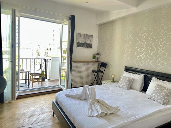 Habitación de hotel con cama, escritorio, silla y balcón con vistas a la ciudad.