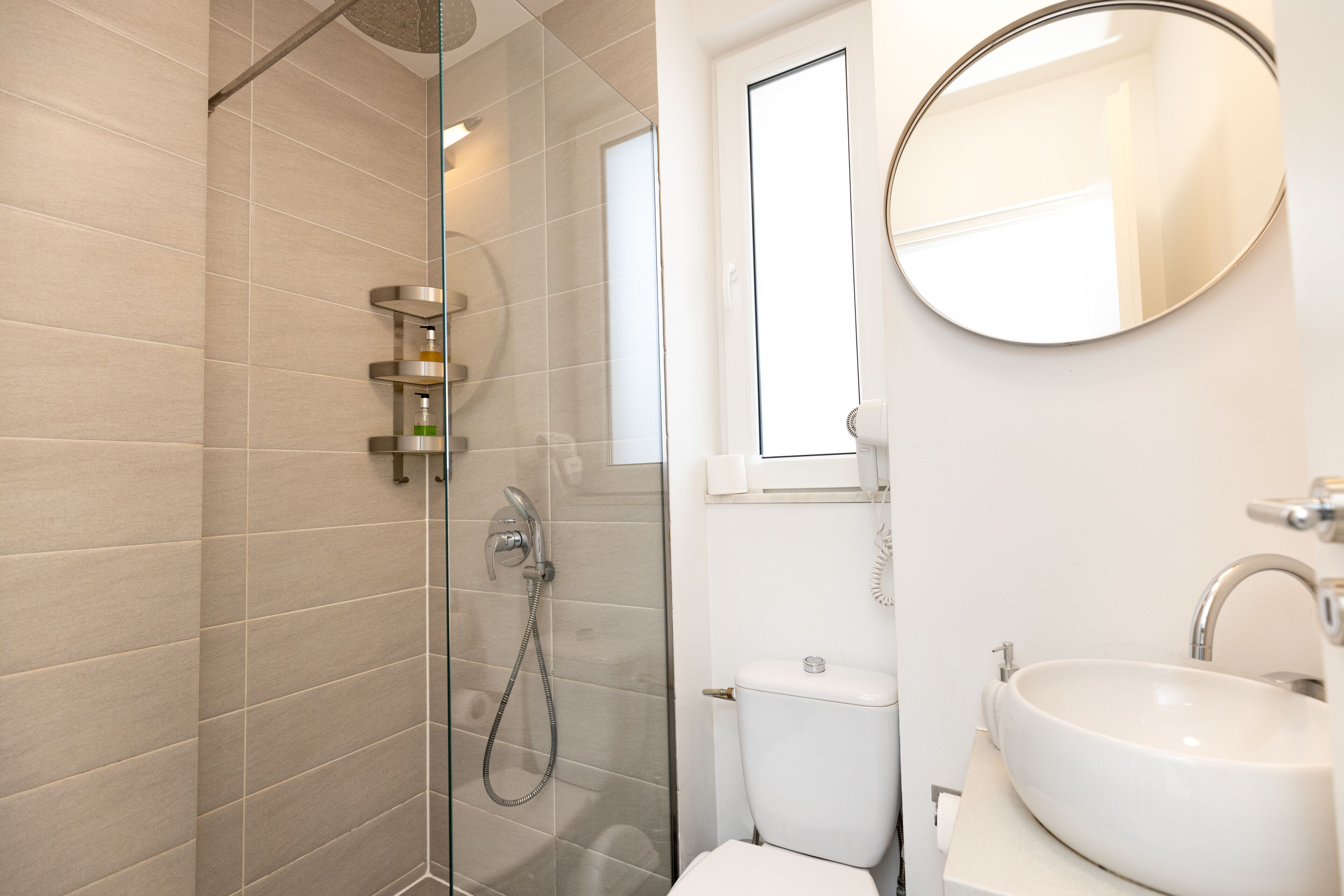 Un baño moderno con ducha de vidrio, inodoro y lavamanos con espejo.