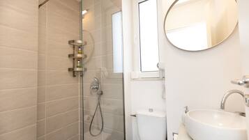 Un baño moderno con ducha de vidrio, inodoro y lavamanos con espejo.