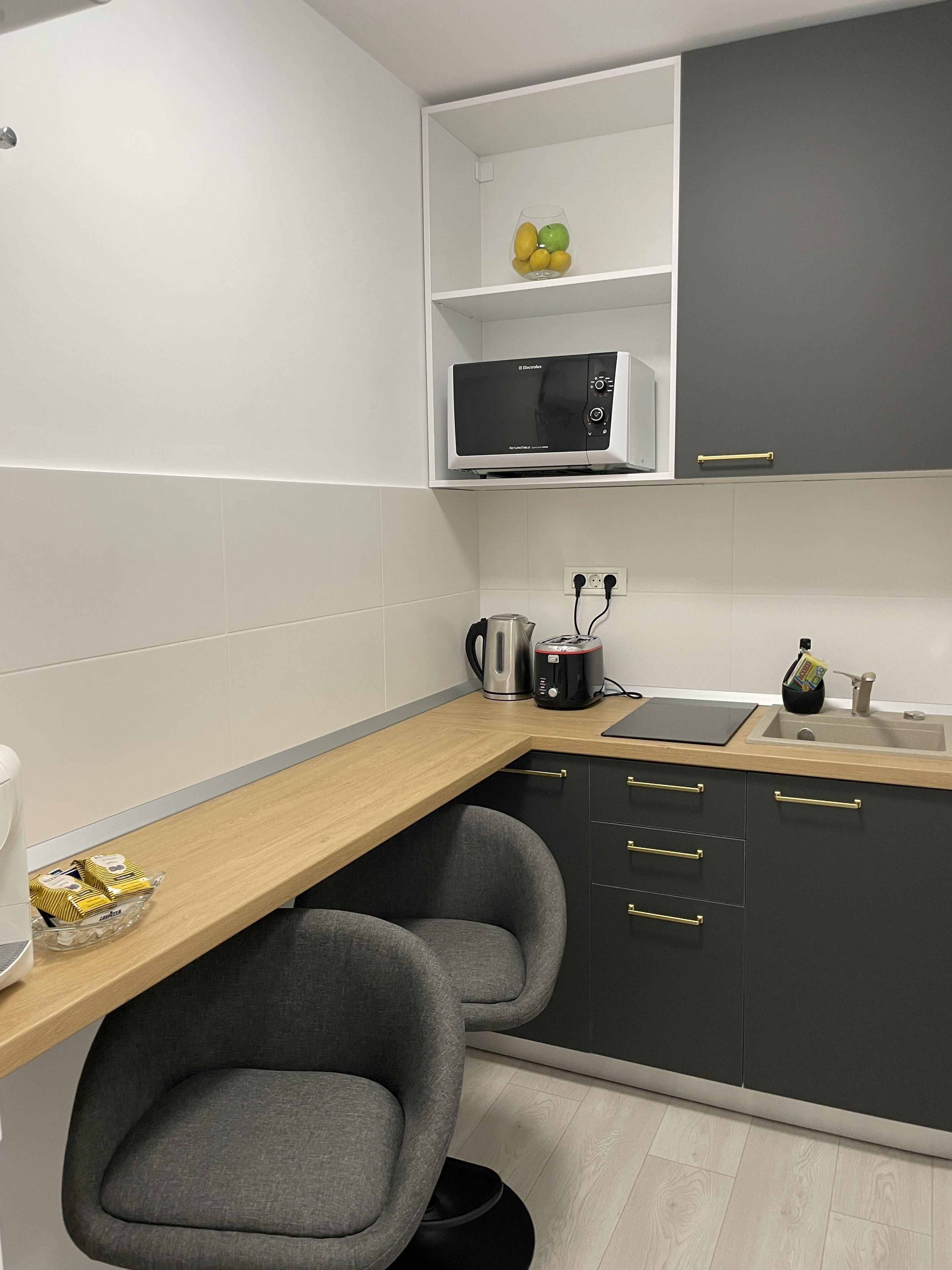 Eine moderne Küche mit einer Mikrowelle, einem Wasserkocher und einem Toaster auf der Arbeitsfläche, einem Spülbecken und einem Stuhl unter der Arbeitsplatte.