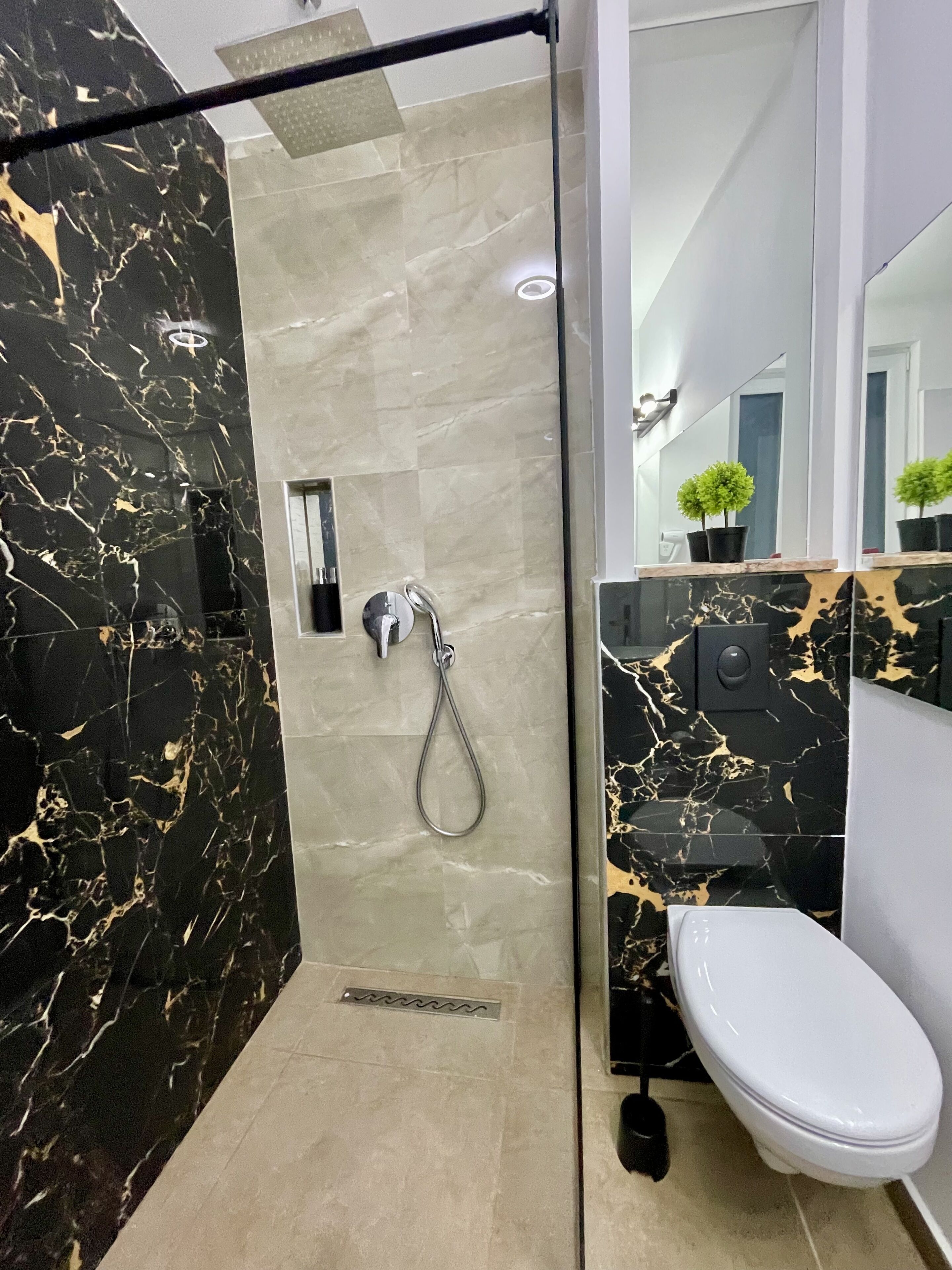 A modern bathroom with a glass-enclosed shower, a toilet, and a sink with a marble countertop.