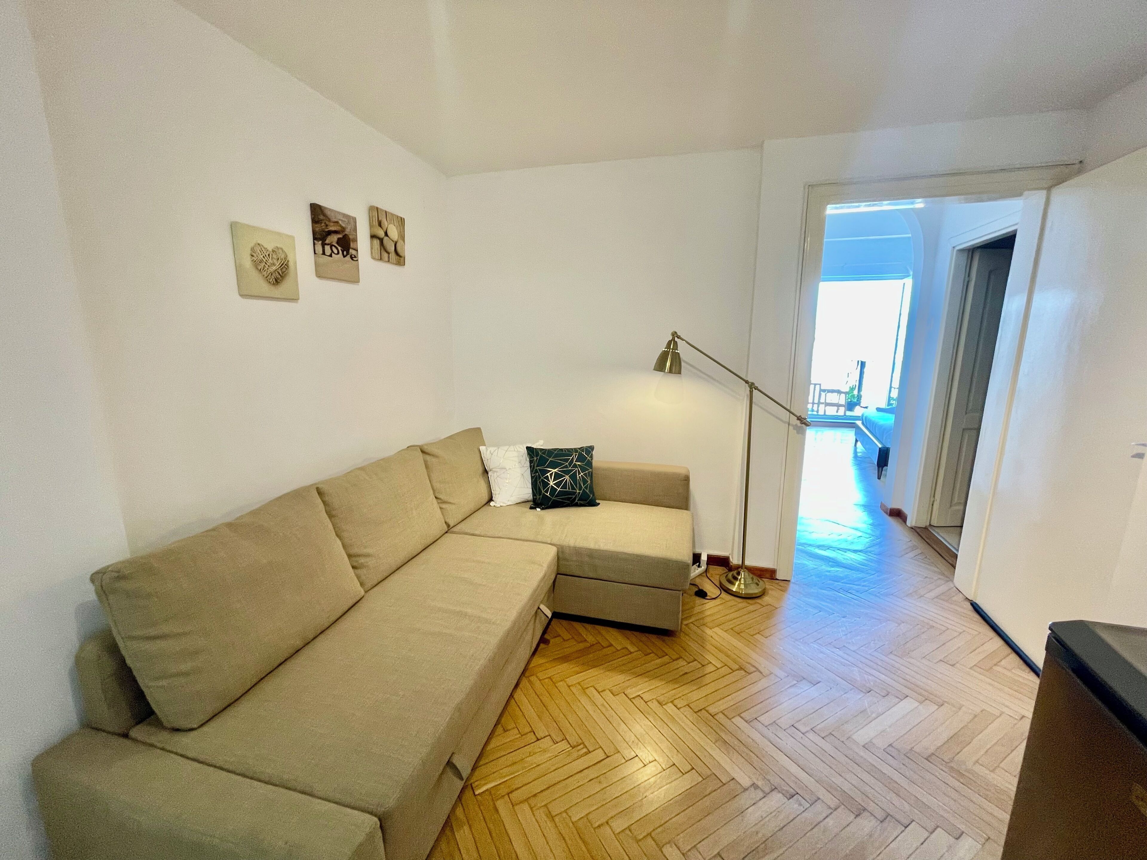 A living room with a beige sectional sofa, a floor lamp, and a herringbone wooden floor.