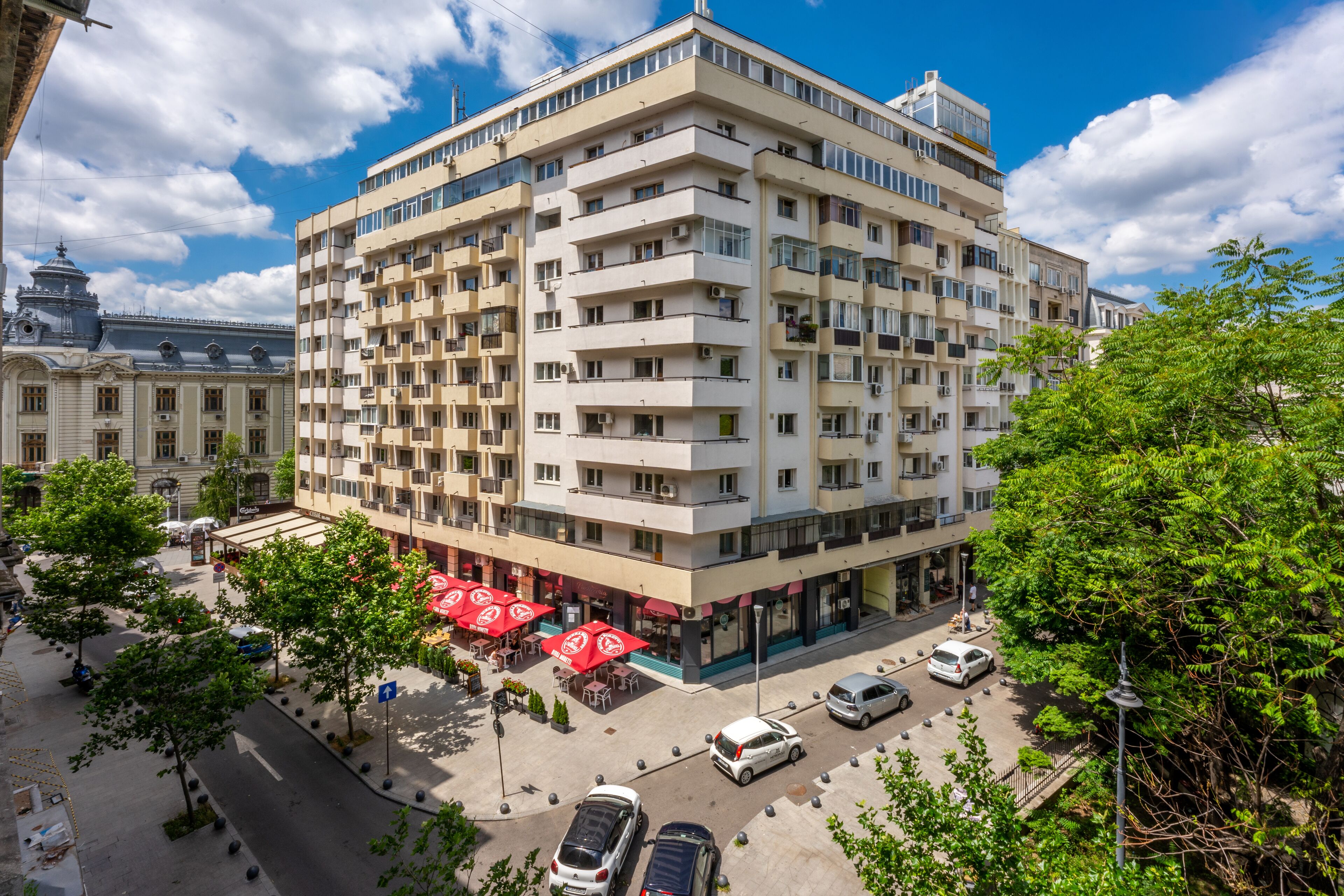 A multi-story hotel with a central courtyard, outdoor seating, and a parking area.