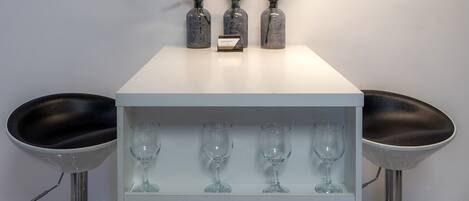 A bar area with three glass vases with lavender flowers, a small card, and four wine glasses on a white shelf.