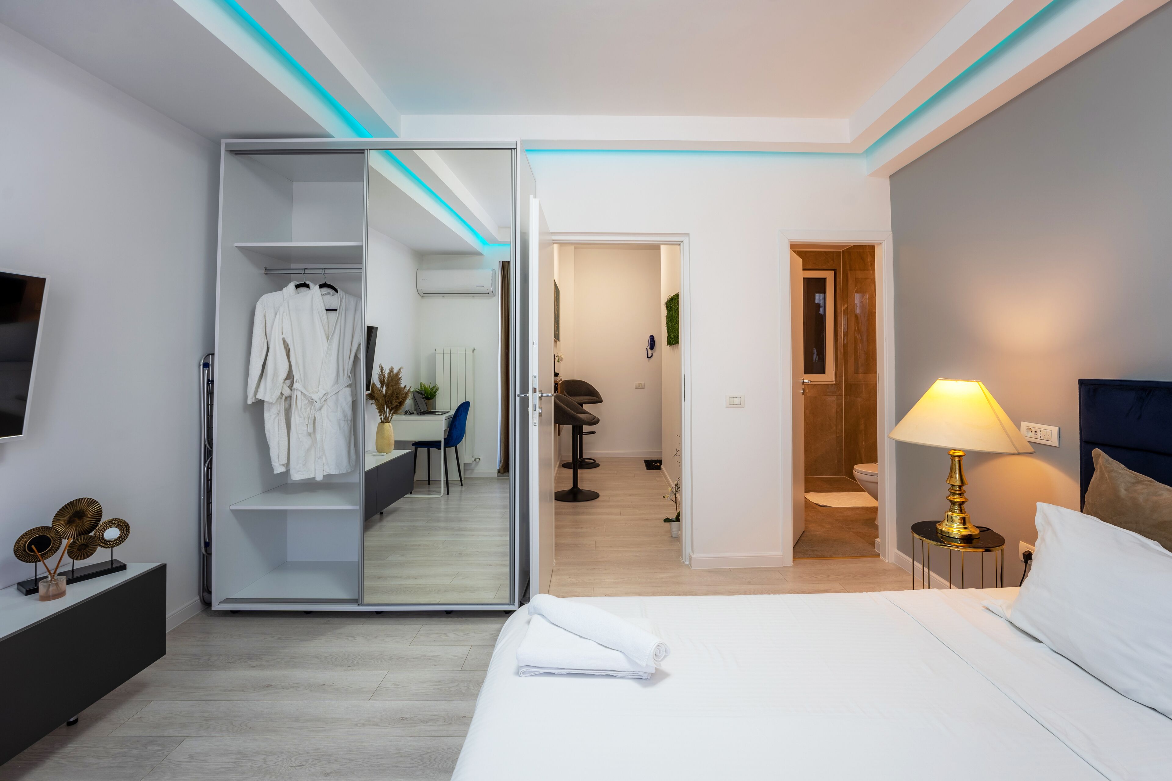 Moderni hotellihuone, jossa on sänky, yöpöytä lampun kanssa, peilillä varustettu vaatekaappi ja kylpyhuone, joka näkyy avoimesta ovesta.