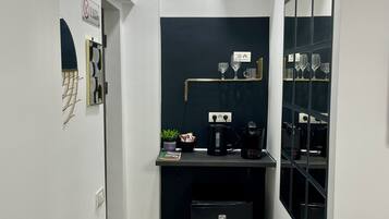 A compact kitchen with a built-in coffee maker, a small trash bin, and a shelf with glasses.