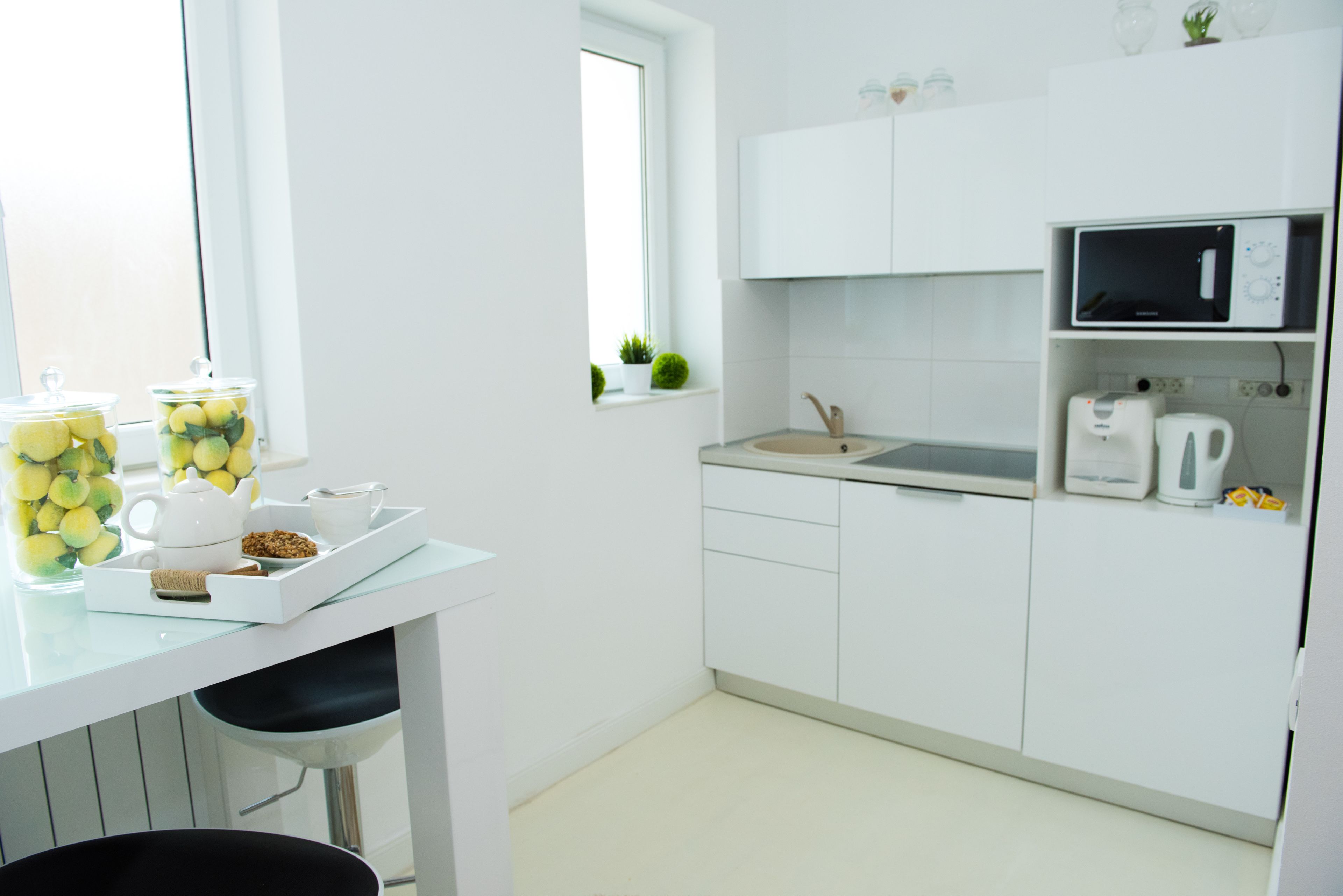Una cocina moderna con armarios blancos, un microondas, un hervidor y una ventana con una planta.