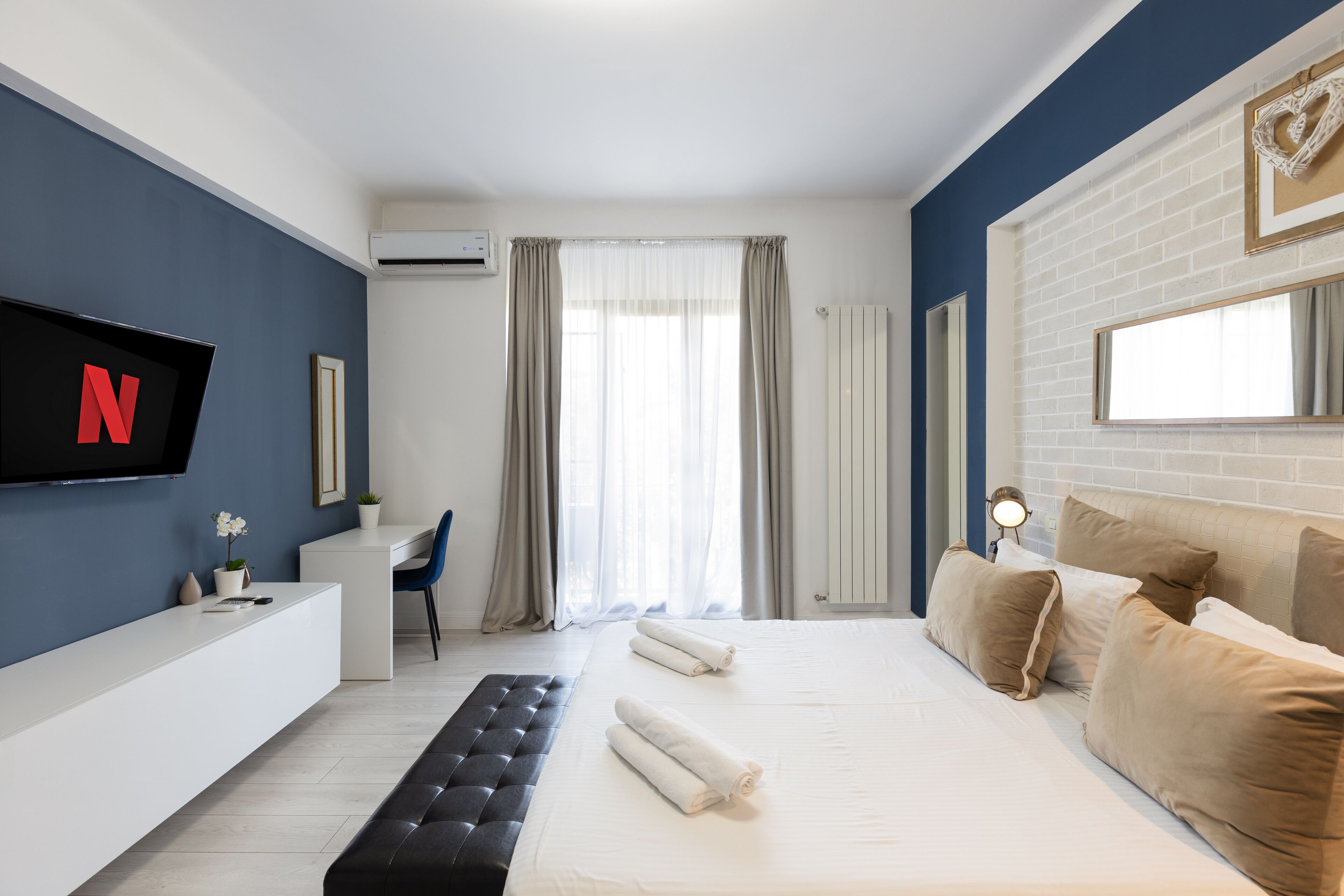 Une chambre d’hôtel moderne avec un grand lit, un bureau, une chaise et un téléviseur affichant le logo de Netflix.