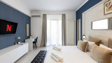 Une chambre d’hôtel moderne avec un grand lit, un bureau, une chaise et un téléviseur affichant le logo de Netflix.