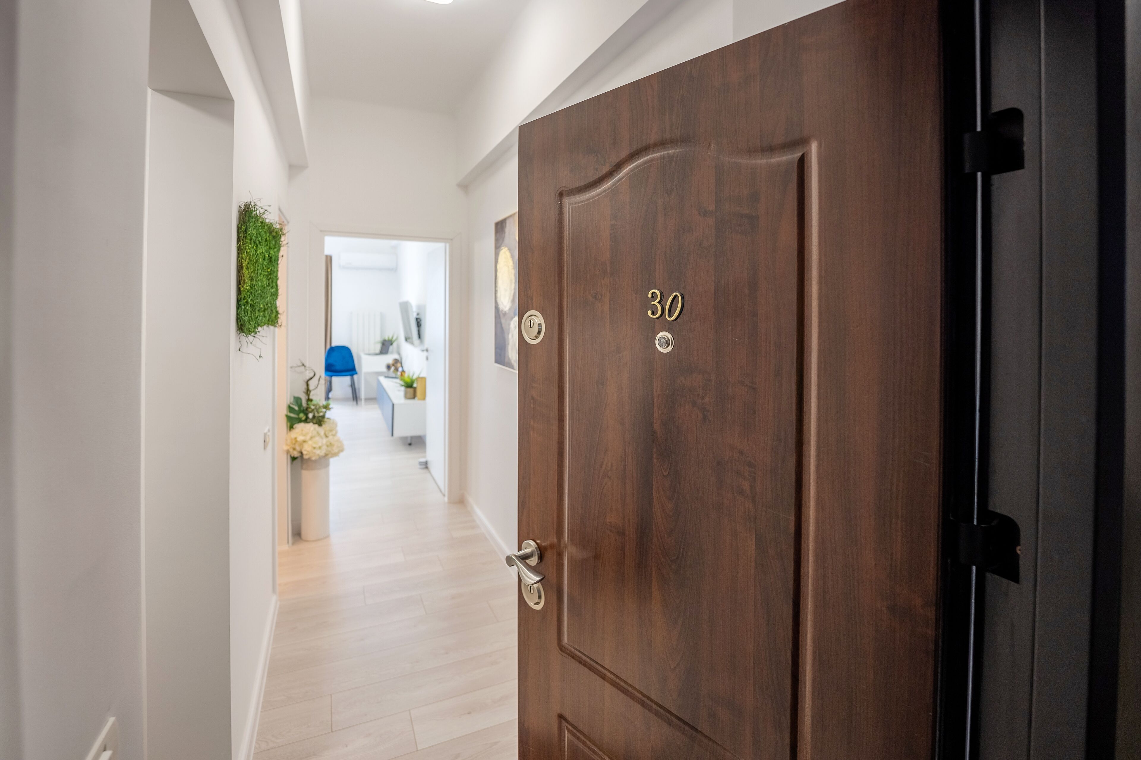 A wooden door with the number 30, a hallway with light-colored flooring, and a blue chair in the background.