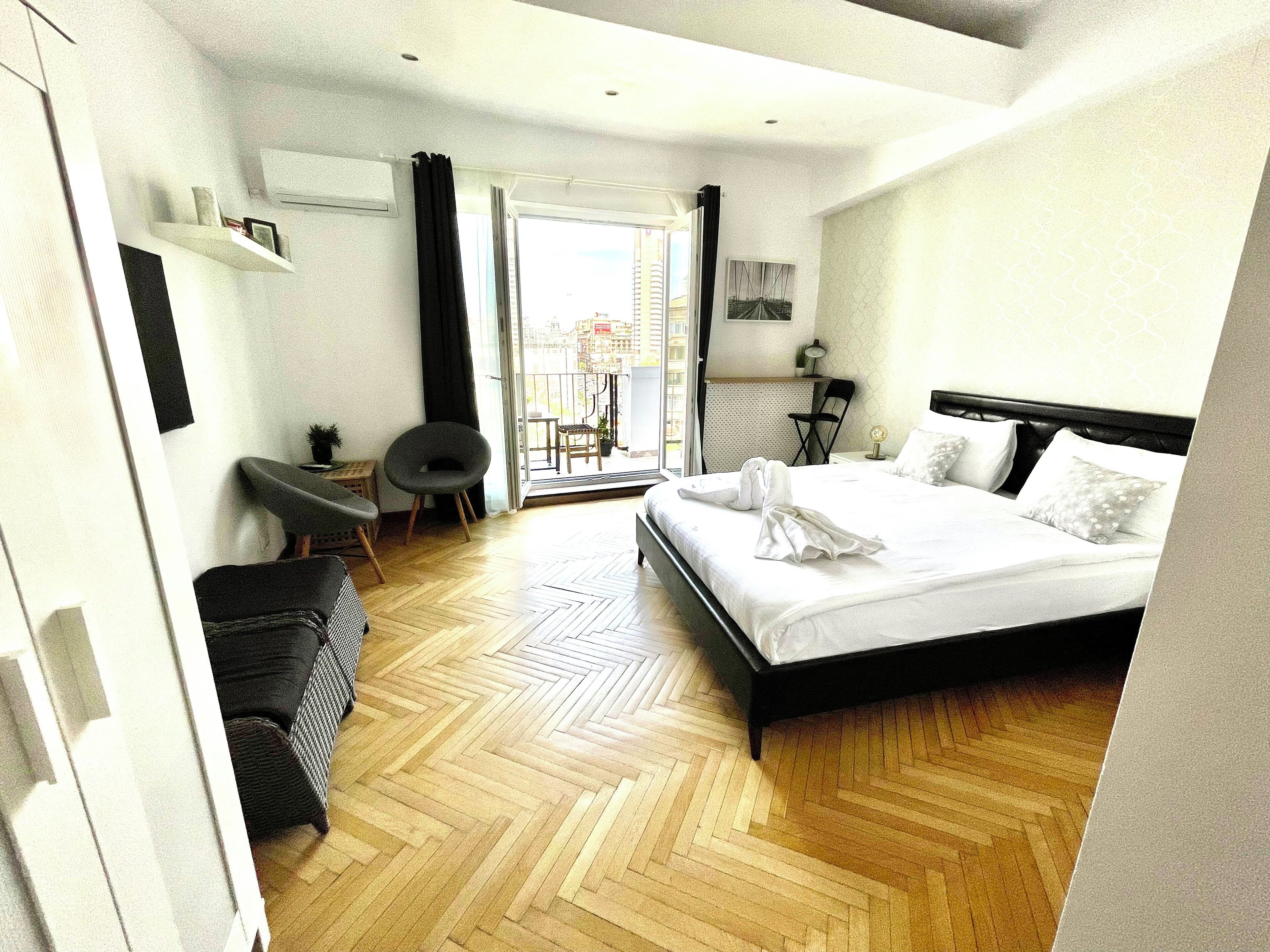 Ein Hotelzimmer mit Bett, Stuhl, Schreibtisch, Topfpflanze und Blick ins Freie.