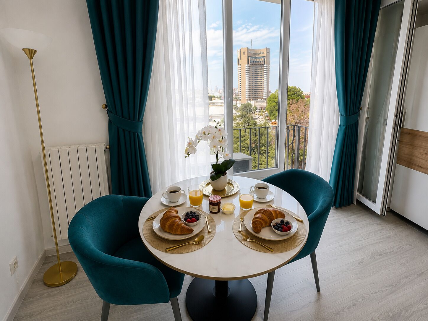 Comedor con una mesa redonda, dos sillas y vistas a un paisaje urbano a través de amplios ventanales.