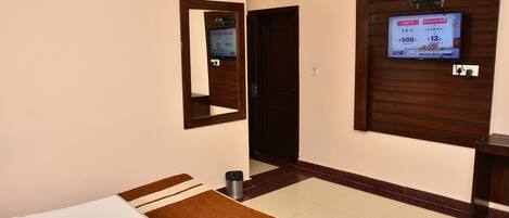 A hotel room with a bed, a TV mounted on the wall, an air conditioning unit, and a wooden door.