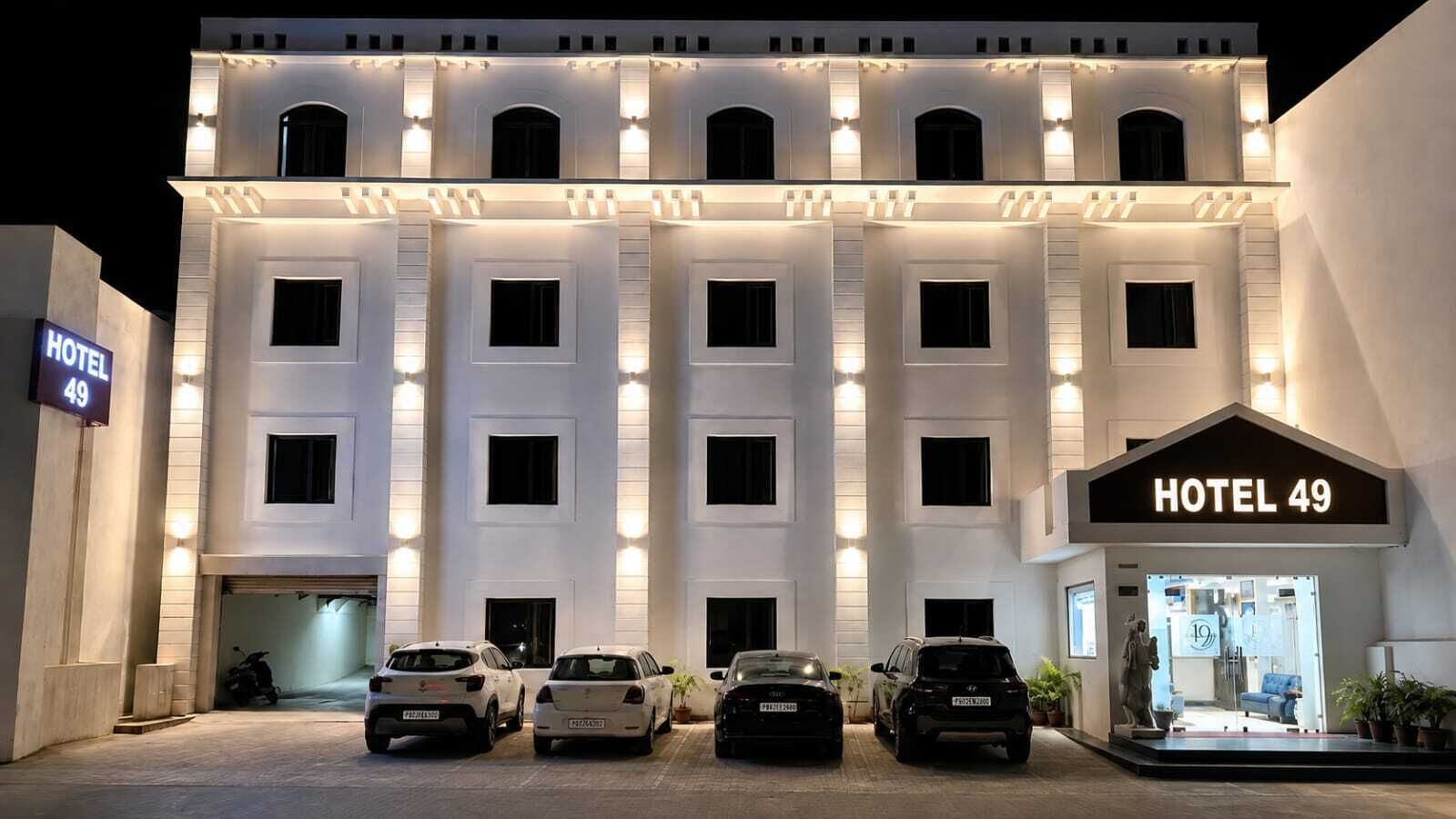 Useita kerroksia sisältävä hotellirakennus, jossa on kyltti, jossa lukee ”HOTEL 49”, ja useita parkkeerattuja autoja sen edessä.