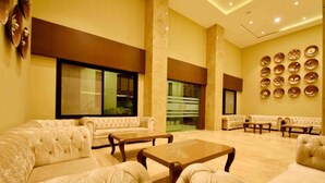 A spacious lobby with plush seating, a large window, and a wall decorated with plates. - Hotel Park Palace (Ujjain)