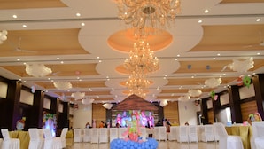 A spacious hall with a high ceiling, chandeliers, and white chairs arranged for an event. - Hotel Park Palace (Ujjain)