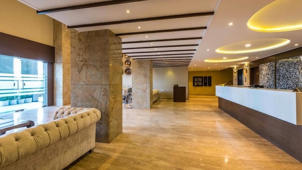 A modern lobby with a marble reception desk, a tufted sofa, and a large pillar. - Hotel Park Palace (Ujjain)