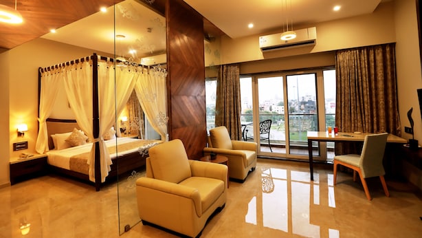 A bedroom with a four-poster bed, a sitting area with chairs, a dining table, and a balcony with a view. - Vits Devbhumi Hotel (Dwarka)
