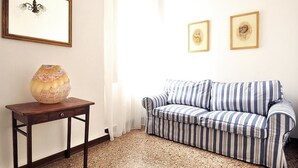 Un salón con un sofá a rayas, una pequeña mesa de madera con un florero y dos cuadros en la pared.