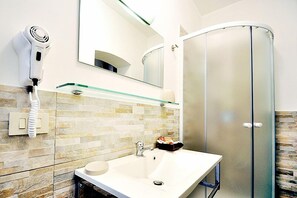 Un baño con lavamanos blanco, repisa de vidrio, secador de pelo y cabina de ducha de vidrio.