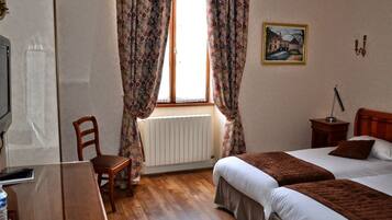 A hotel room with two beds, a radiator, a desk with a chair, and a window with curtains.