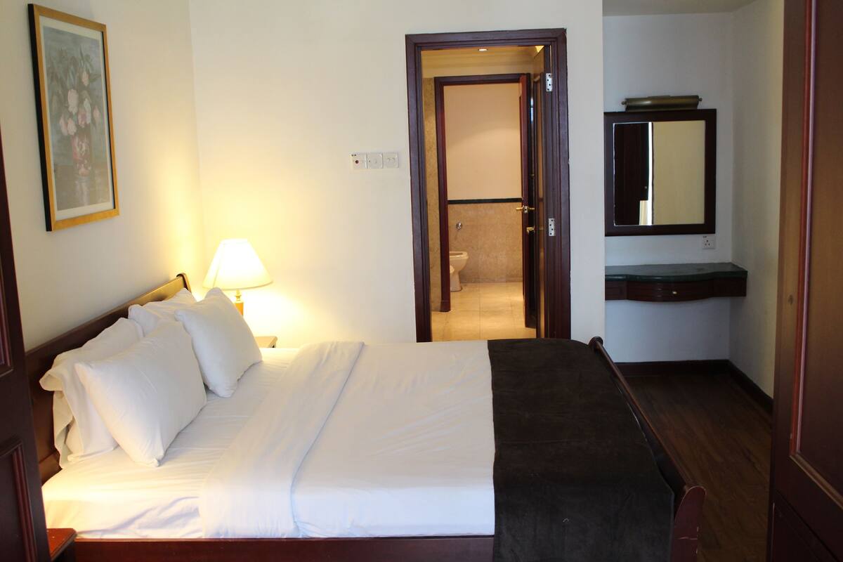 A hotel room with a bed, a bedside lamp, a mirror, and a bathroom visible through an open door.