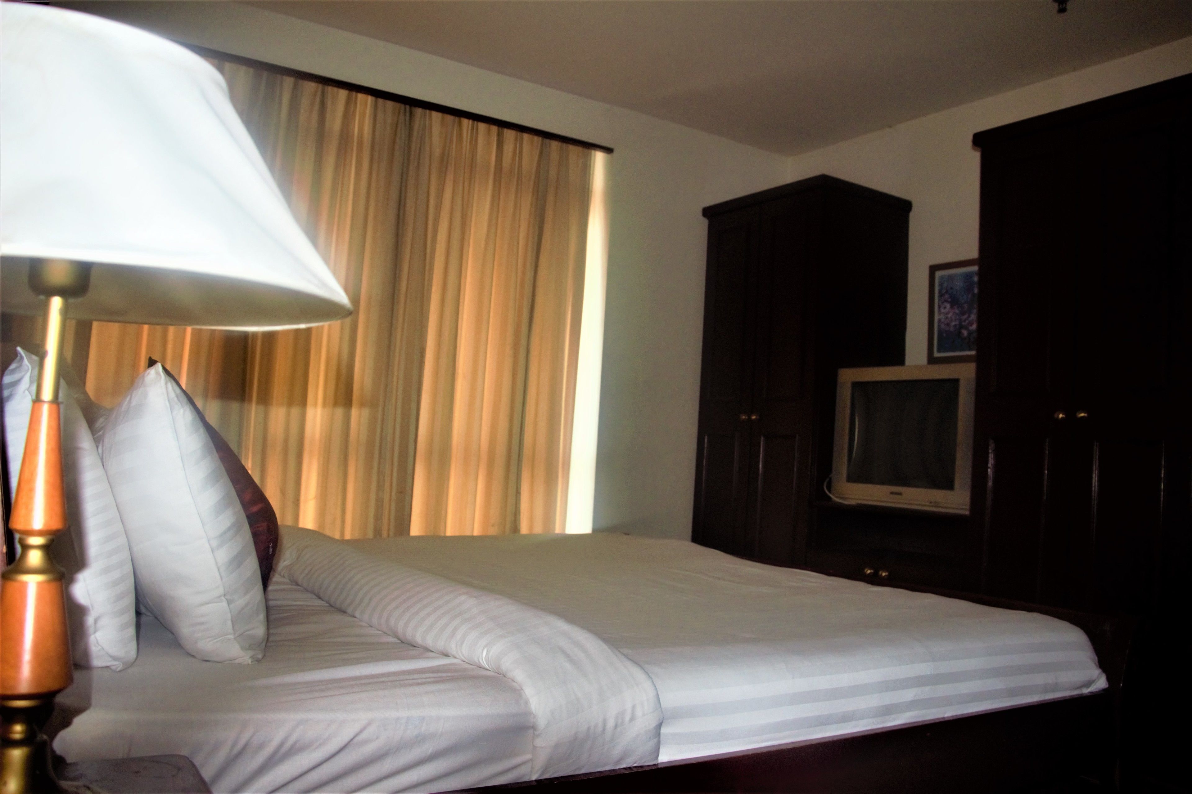 A hotel room with a bed, a lamp, a television, and a window with curtains.