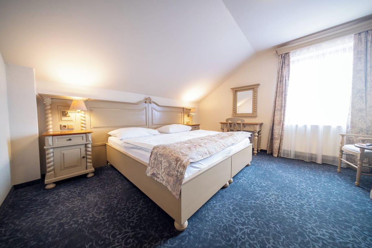 A neatly arranged hotel room with a bed, bedside tables, a chair, and a window with curtains.