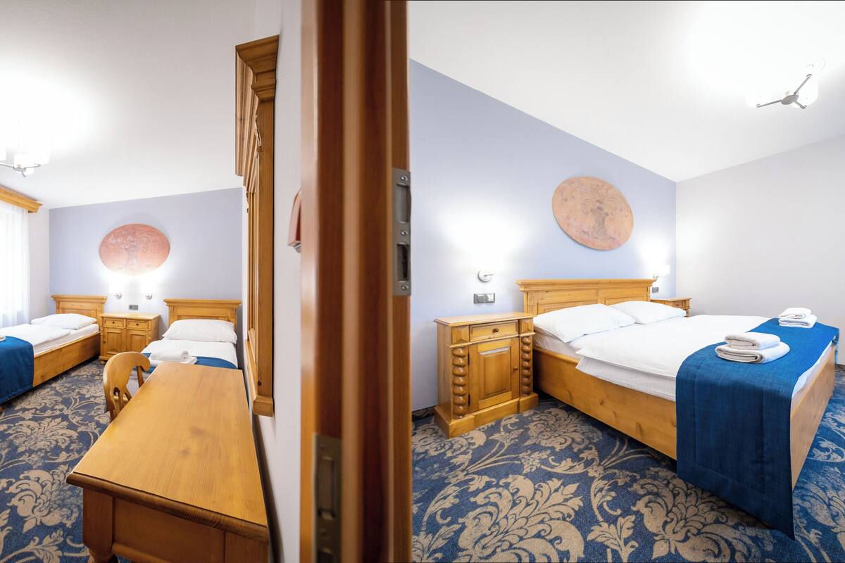 A hotel room with two beds, a wooden desk, a nightstand, a mirror, and a wall-mounted artwork.
