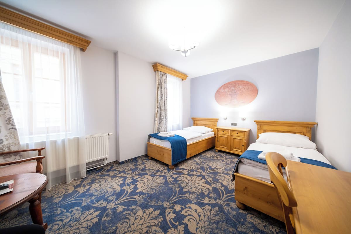 A hotel room with two wooden beds, a wooden chair, a small table, and a radiator.