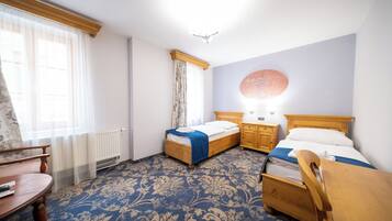 A hotel room with two wooden beds, a wooden chair, a small table, and a radiator.