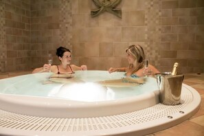 Two people in a hot tub with a champagne bottle and glasses.
