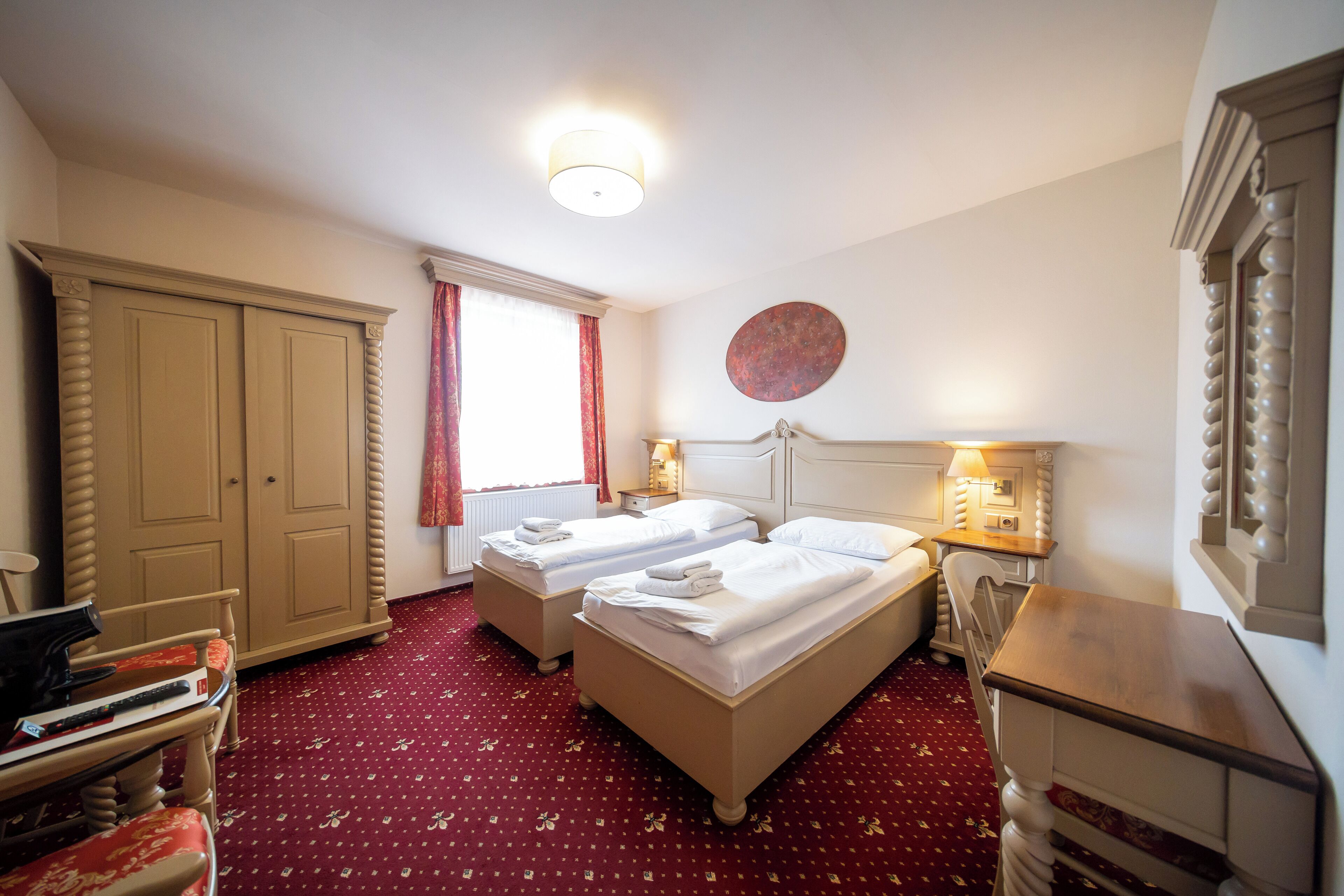 A hotel room with two beds, a desk, a chair, a wardrobe, and a window with curtains.