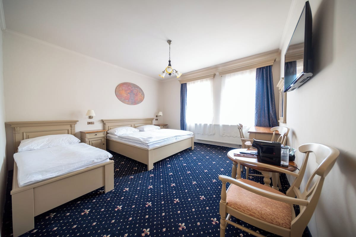 A hotel room with two beds, a desk, a chair, a TV, and a window with curtains.