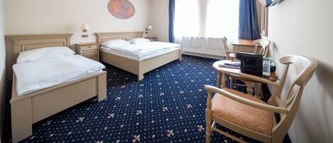 Habitación de hotel con dos camas, un escritorio, una silla, un televisor y una ventana con cortinas.