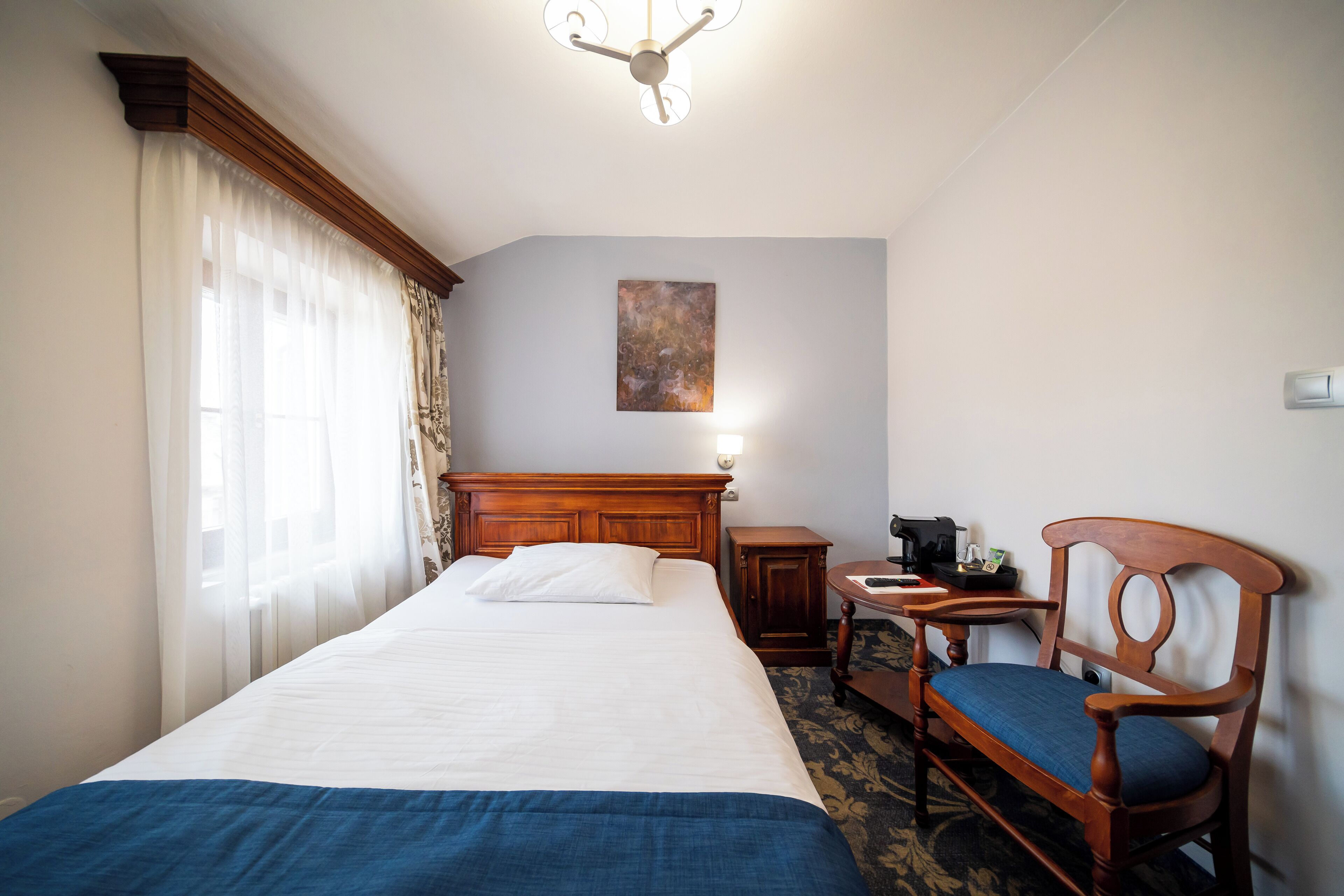 A hotel room with a large bed, a wooden headboard, a desk with a chair, and a painting on the wall.