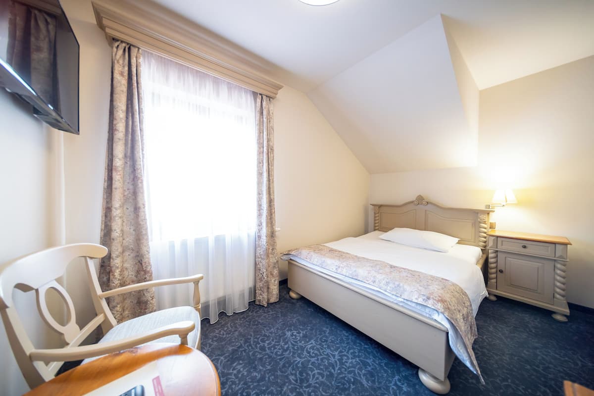 A hotel room with a bed, a chair, a nightstand, and a TV mounted on the wall.