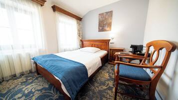 A hotel room with a bed, a chair, a desk, and a radiator.