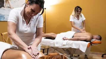 A massage therapy room with a yellow wall, a massage table, and two clients receiving treatment.
