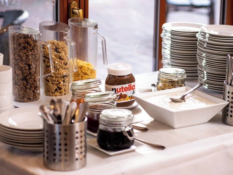 Una mesa de buffet con diferentes alimentos, como granola, cereales y frascos con salsas y untables.