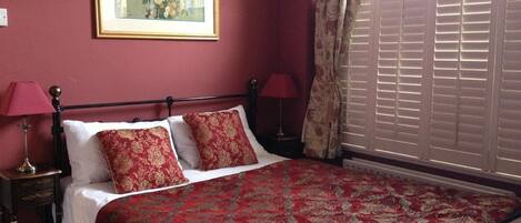 A bedroom with a bed, two bedside tables, a nightstand, a window with blinds, and a framed picture on the wall.
