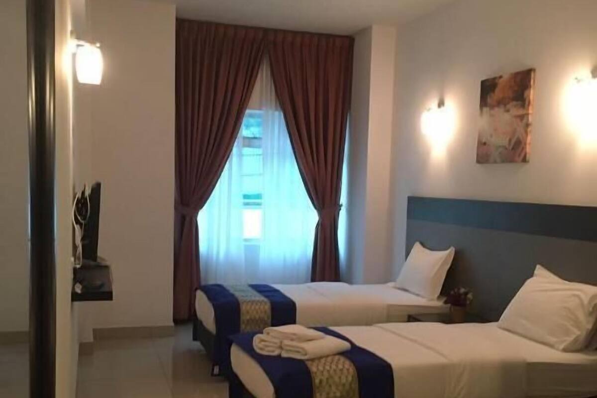 Habitación de hotel con dos camas, una ventana con cortinas, una lámpara de pared y un cuadro.