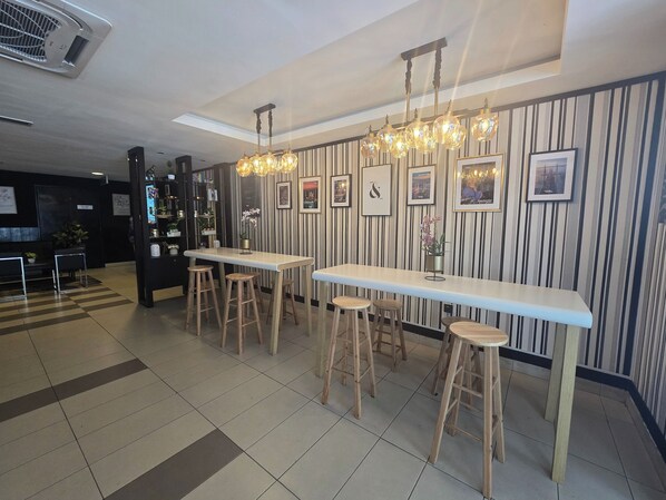 A modern bar area with striped wallpaper, multiple stools, and pendant lighting.
